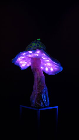 Leuchtende Fliegenpilz Skulptur mit LED Beleuchtung unter dem Hut. Der Pilz ist gelb mit blauen Flecken.