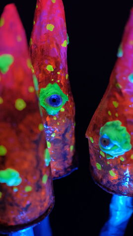 Drei leuchtende Pilz Skulpturen mit spitzem Hut und Augen im UV-Licht