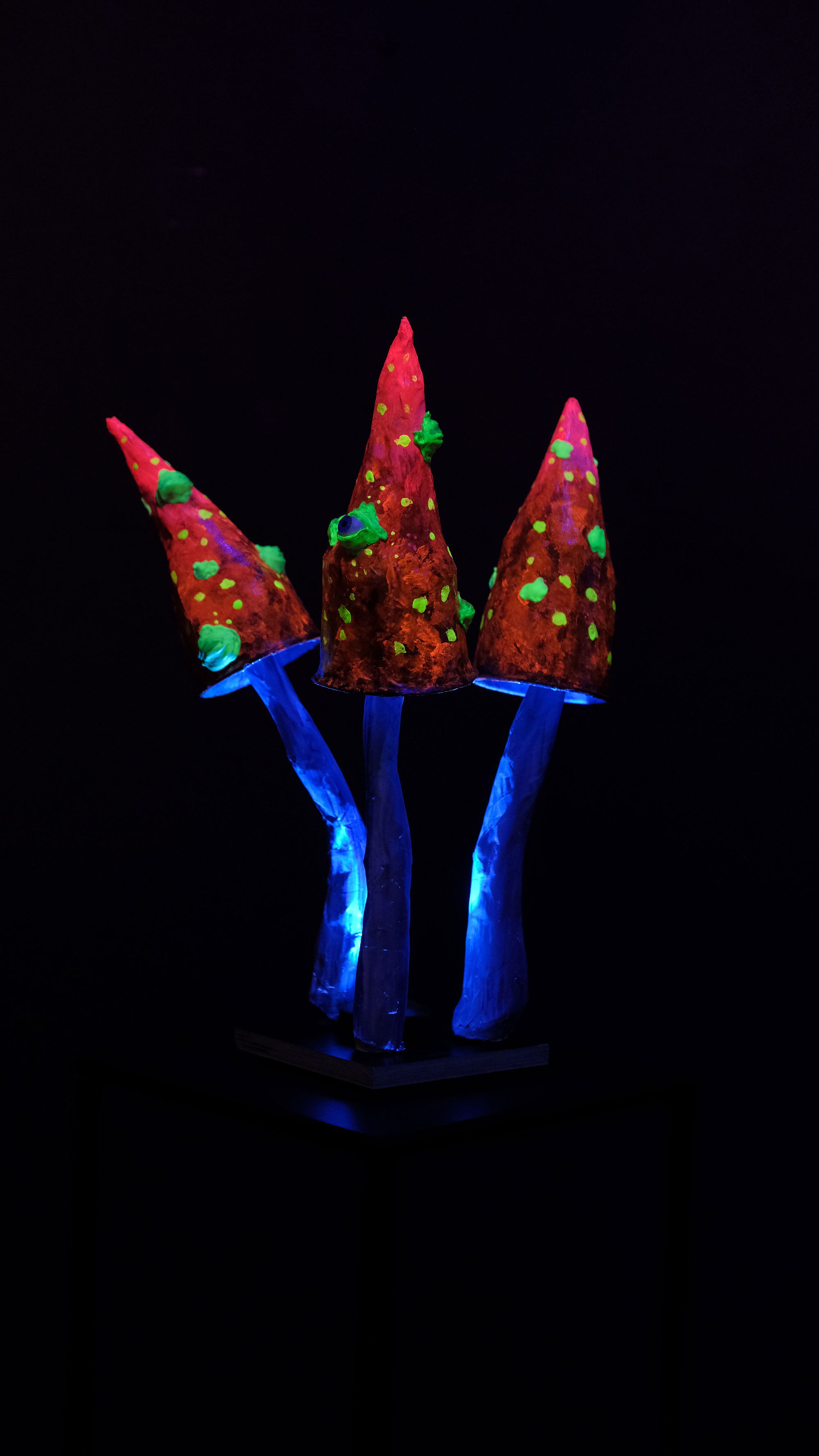 Drei leuchtende Pilz Skulpturen mit spitzem Hut und Augen im UV-Licht