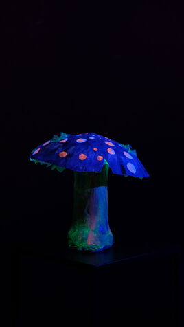 Leuchtende Pilz Skulptur mit flachem, blauem Hut und Augen im UV-Licht
